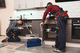 Two repairmen uninstalling a used appliance in a kitchen